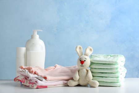 Stack of diapers and baby accessories on table against color background. Space for text